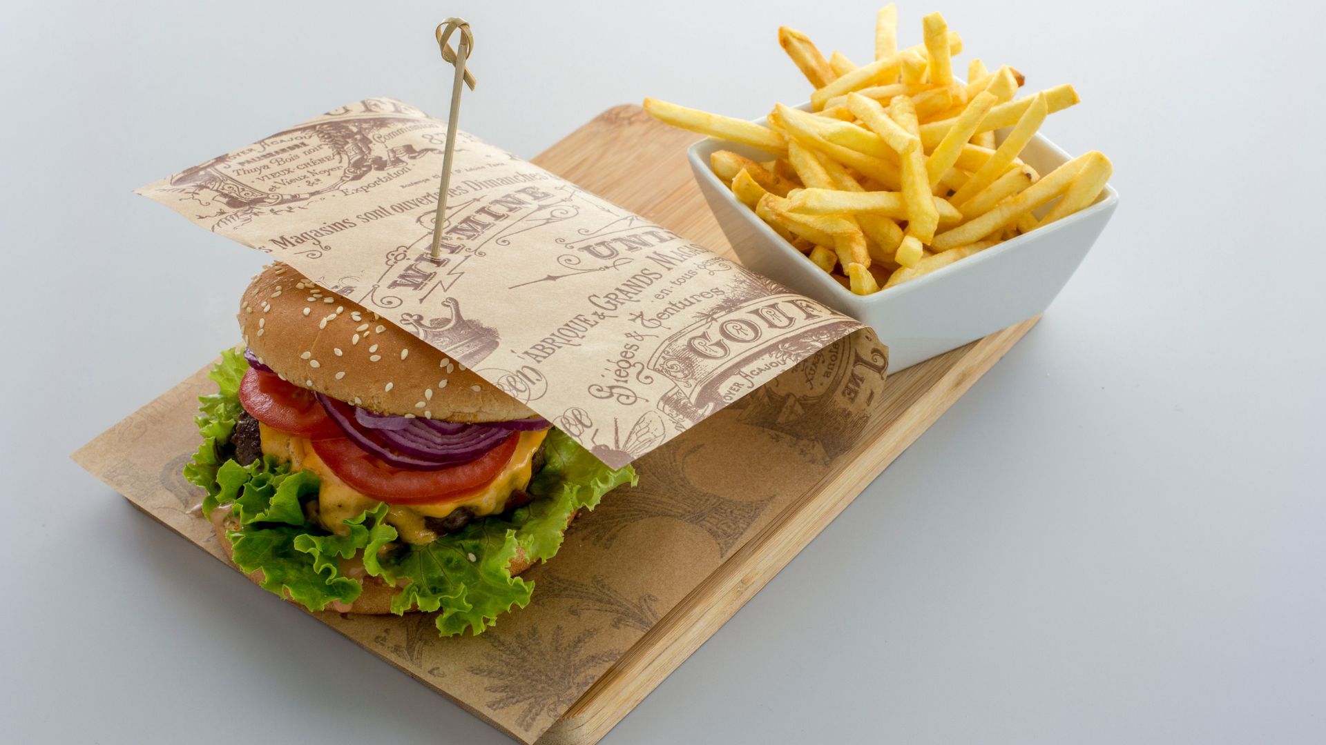 A hamburger in wrapping paper and fries in a bowl